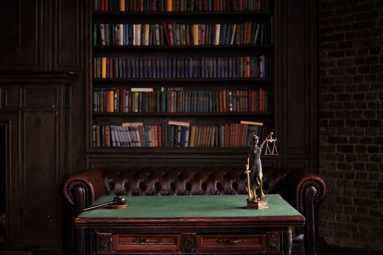 Home A classic study room with shelves of books, a gavel, and Lady Justice figurine on a green table.