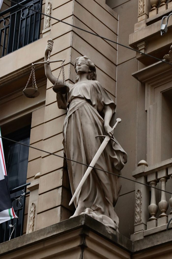 A stone statue of Lady Justice stands on the facade of a historic building, symbolizing law and order.